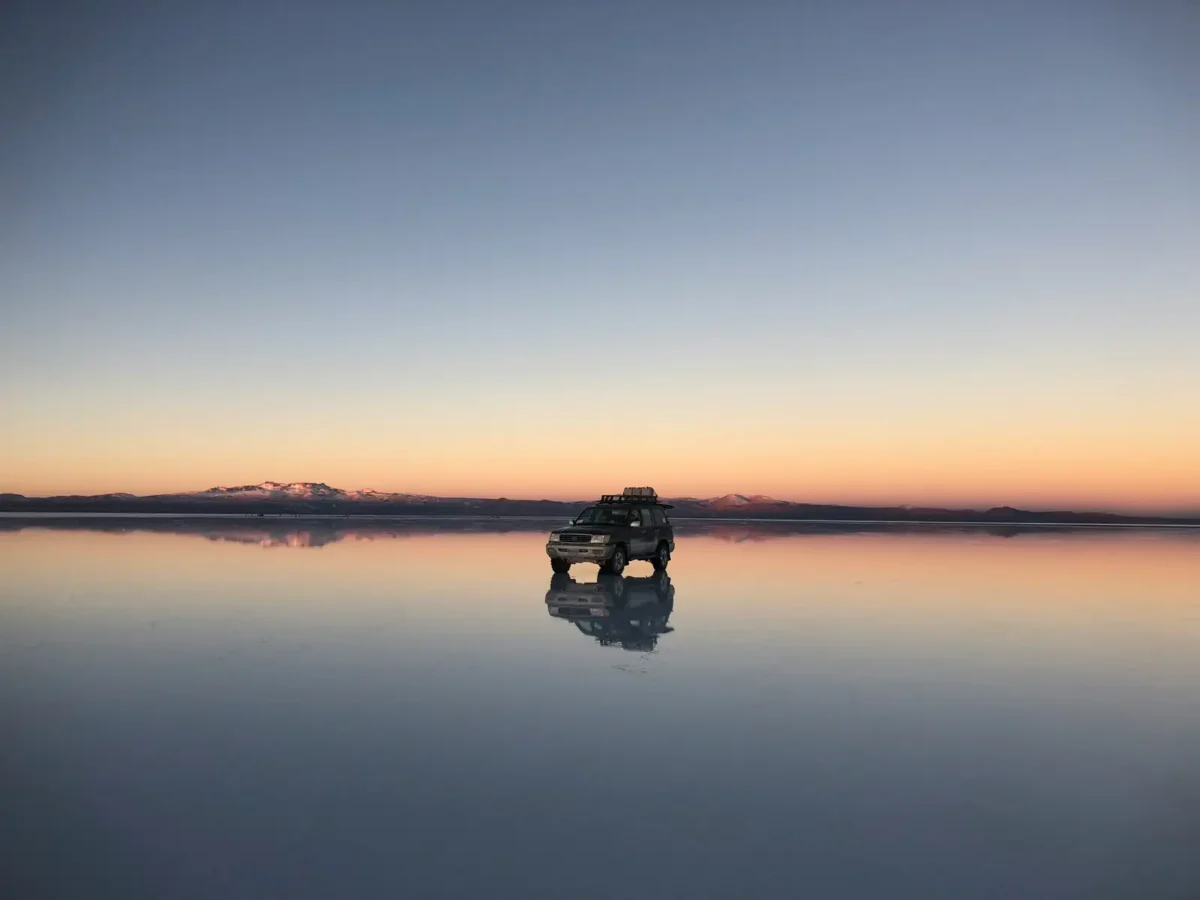 4x4 jeep reflected on the flooded Salar de Uyuni at dusk